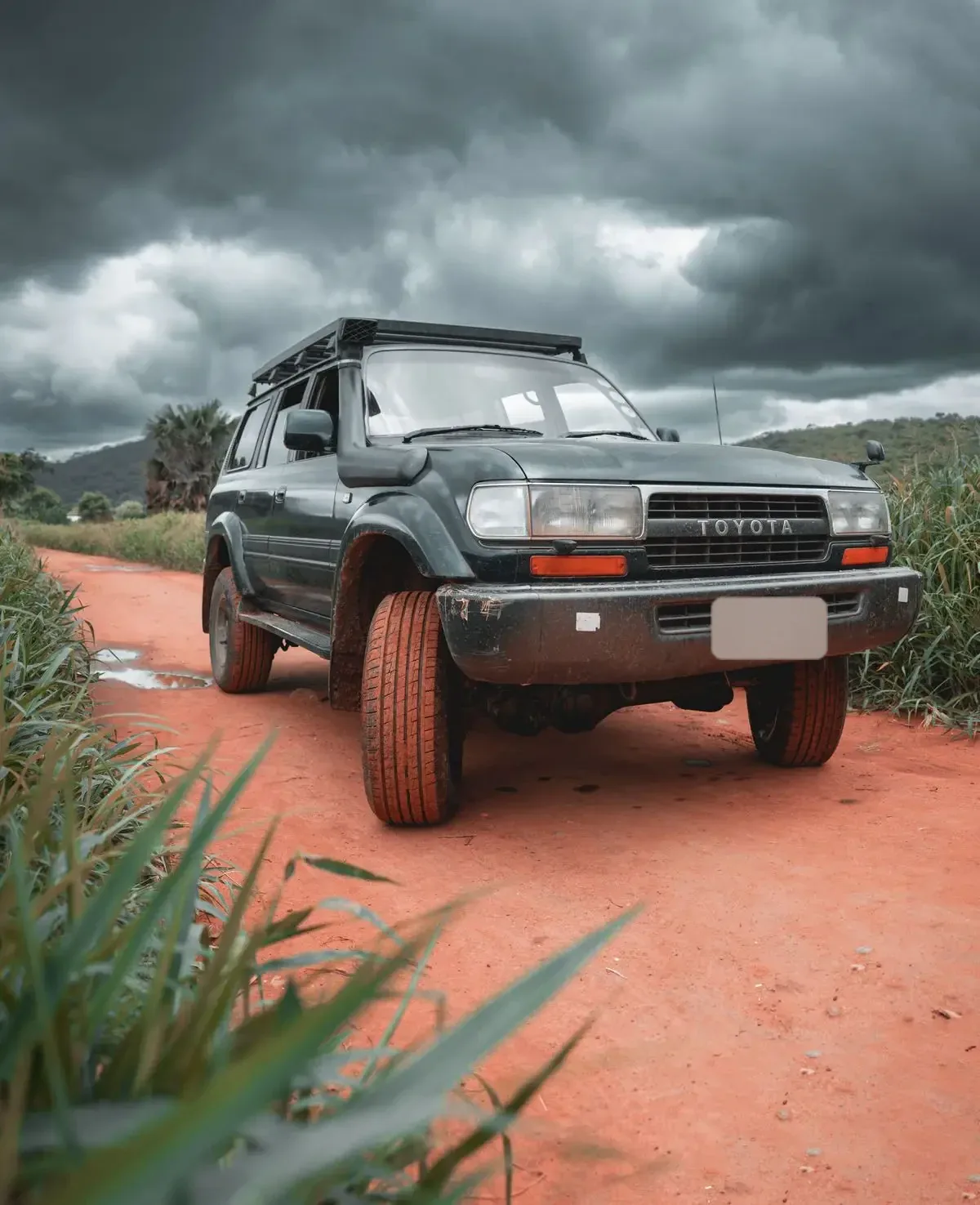 Toyota Land Cruiser série 80 sur une piste rouge sous un ciel d'orage